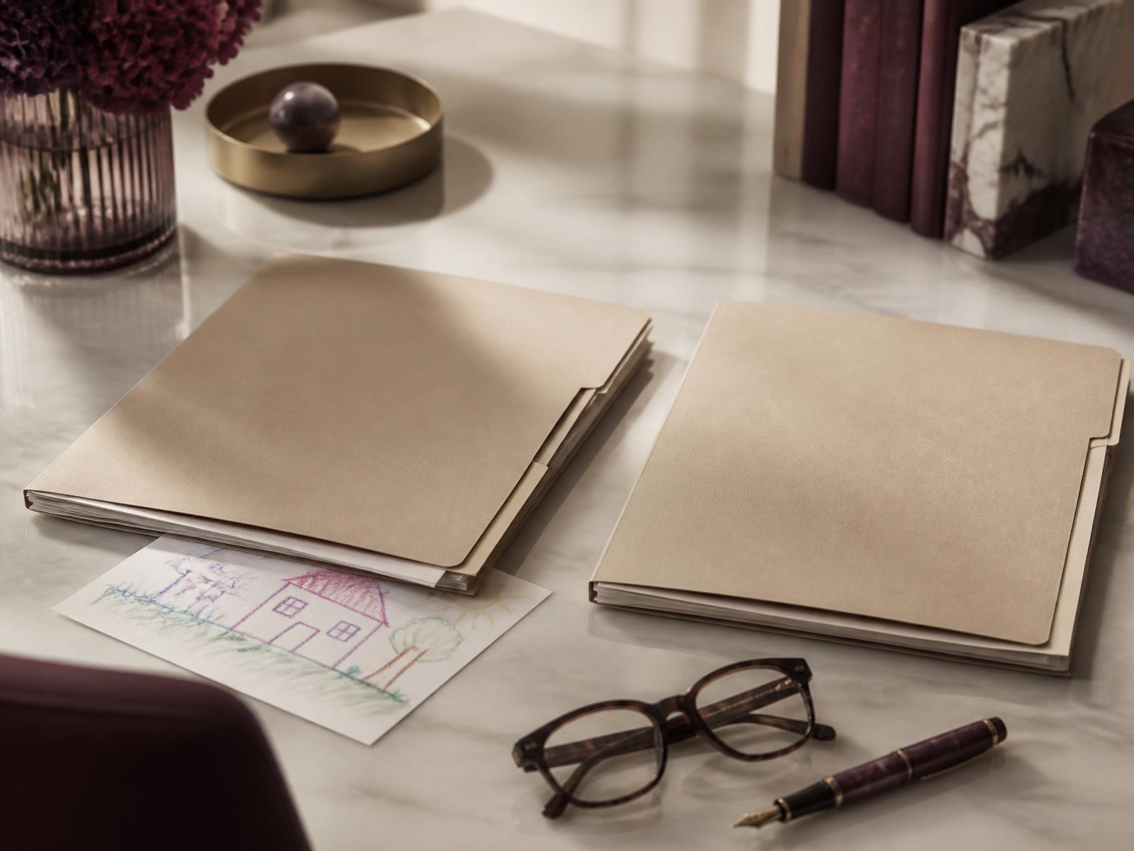 Two identical candidate folders side by side on a marble desk, one resting on a child's crayon drawing